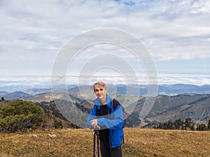 Young male hiker with trekking poles and backpack standing on a mountain ridge