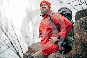 Young male hiking in mountains wearing red clothes exploring new place. Traveler bearded man trekking and mountaineering