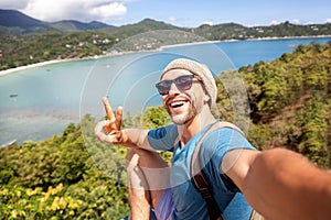 Young male hipster traveler doing selfie overlooking the tropical sea. Adventure, vacation, wonderlust, internet, technology