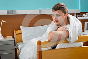 Young male ill patient leaning on the hospital bedstead covered