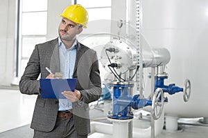 Young male inspector writing on clipboard while looking away in industry