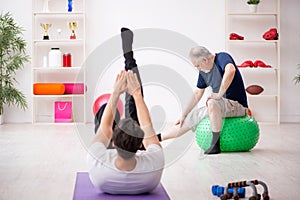 Young male instructor and old man doing sport exercises