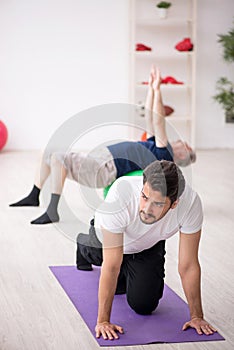 Young male instructor and old man doing sport exercises