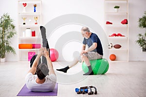 Young male instructor and old man doing sport exercises