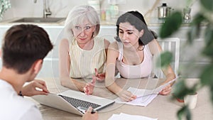Young male insurance agent offers the best insurance terms for an elderly woman and her adult daughter.