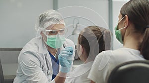 A young male laboratory assistant takes a swab from the nasopharynx of a little girl for analysis on covid-19, she is