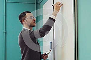 Young male lecturer writes on whiteboard in classroom