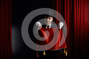 Young male magician actor showing trick with napkin in mysterious atmosphere