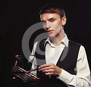 Young male make up artist holding shadow palette and brush.