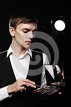 Young male make up artist holding shadow palette and brush.