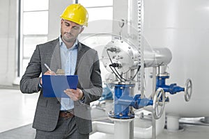 Young male manager writing on clipboard in industry