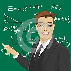 Young male math teacher with piece of chalk standing next to blackboard