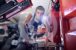 young male mechanic looking at engine with torch