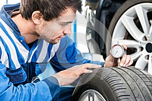 Young Male Mechanic Pressing Gauge Into Tire In Garage