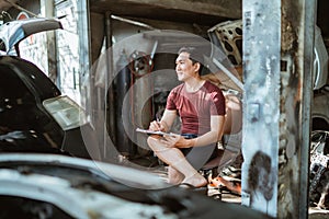 young male mechanic sits recalling while writing a list of car repairs photo