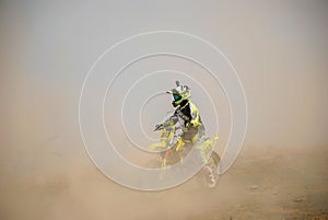 Young male motorcyclist wearing a bright yellow helmet and protective gear riding a dirt bike
