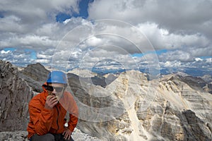 Young male mountain climber on a Dolomite mountain peak enjoying the view and eating a sandwich