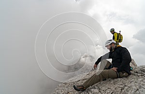 Young male mountain climber on a Dolomite mountain peak enjoying the view with his guide standing behind