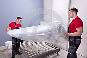 Young Male Movers Placing The Mattress Over The Bed