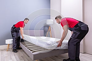 Young Male Movers Placing The Mattress Over The Bed