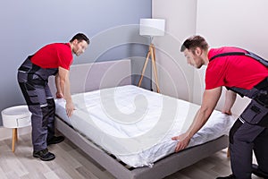 Young Male Movers Placing The Mattress Over The Bed