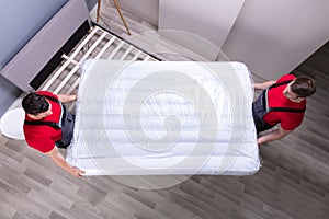 Young Male Movers Placing The Mattress Over The Bed