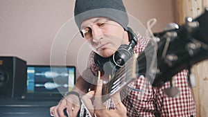 Young male musician composes and records soundtrack playing the guitar using computer, headphones and keyboard