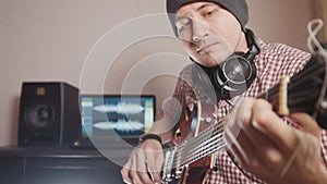 Young male musician composes and records soundtrack playing the guitar using computer, headphones and keyboard