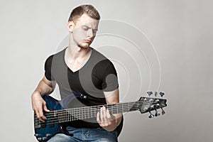 Young male musician playing a six-string bass guitar isolated