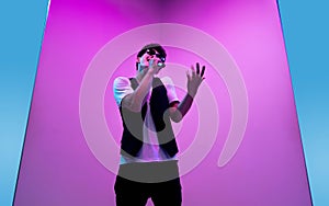 Young male musician, singer performing on pink-bluebackground in neon light