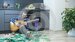 Young male musician watching online guitar lessons and trying to play new chords. Man sitting at home in kitchen and playing on ac