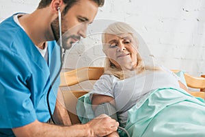 young male nurse measuring blood pressure to senior woman