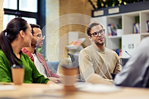 Young male office worker discussing something with multiracial colleagues while working together in the modern office