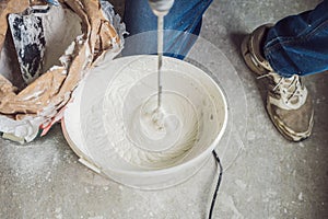 Young male painter kneads putty with water in a bucket using a hand-held mixer for building mixes