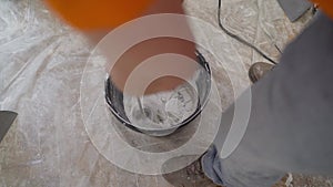 a young male painter kneads putty with water in a bucket using a hand-held mixer for building mixes. Worker mixes water