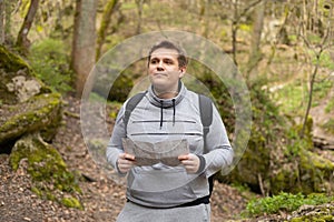 Young male with paper map hiking on the road in nature. 30s men in sport clothes walking on woodland. Guy portrait