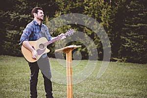 Young male in a park holding a guitar and playing a song from the Christian hymn book