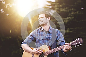 Young male in a park holding a guitar and playing a song from the Christian hymn book