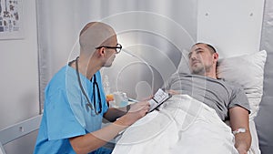 Young Male Patient Talking To Consultant In Emergency Room. Doctor examines a patient and takes notes in a notebook