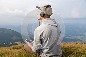 Young male person enjoys music in headset from cell phone in mountains