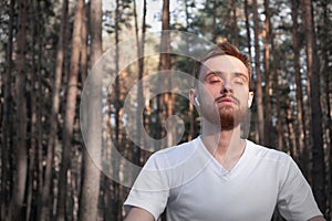 Young male person meditating in the forest using modern technology.