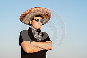 Young male person in sombrero and sunglasses in clear sky background. Mexico independence festive concept of man wearing national