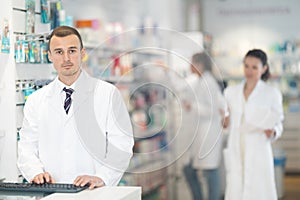 Young male pharmacist standing at the desk using keyboard in chemist's shop