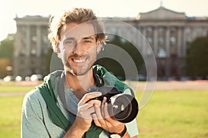 Young male photographer holding professional camera on street.