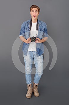 Young male photographer in jeans jacket studio isolated on grey with camera surprised