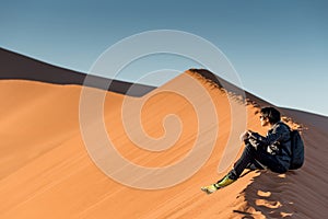 Young male photographer sitting on sand dune, Namibia