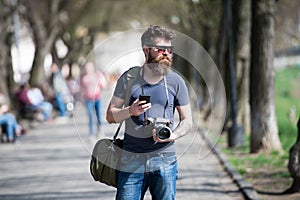 Young male photographer stroll around city in search for perfect picture. Bearded man in stylish eyewear holding vintage