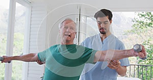 Young male physiotherapist helping retired senior man exercising with dumbbells at nursing home