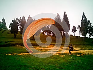 Young male pilot of a orange paraglider doing ground handling on the hill on a cloudy day in Delo Park, Kalimpong, India photo