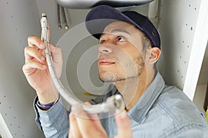 young male plumber fitting flexible pipe under sink